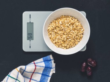 Diyet kavramı, doğru beslenme, sağlıklı yemek. Yulaf ezmesi mutfak terazisi üzerinde beyaz bir tabak içinde. Ürünler ağırlığında. Kahvaltı, üstten görünüm