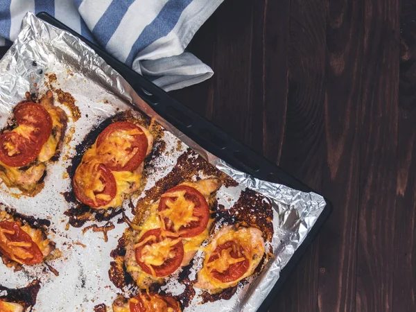 Domates ve peynirle bir fırın tepsisine folyo ile tavuk fileto pişmiş. Lezzetli sağlıklı gıda. Bir yaşam tarzı. Düz yatıyordu. Üstten görünüm. Ahşap arka plan