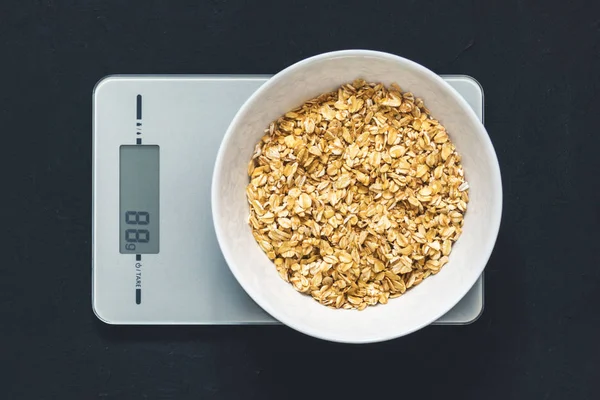 Diyet kavramı, doğru beslenme, sağlıklı yemek. Yulaf ezmesi mutfak terazisi üzerinde beyaz bir tabak içinde. Ürünler ağırlığında. Kahvaltı, üstten görünüm