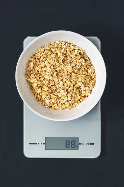Diyet kavramı, doğru beslenme, sağlıklı yemek. Yulaf ezmesi mutfak terazisi üzerinde beyaz bir tabak içinde. Ürünler ağırlığında. Kahvaltı, üstten görünüm