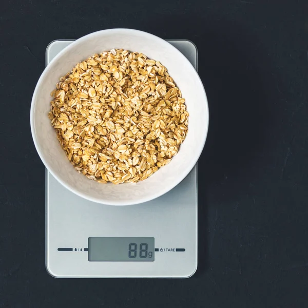 Diyet kavramı, doğru beslenme, sağlıklı yemek. Yulaf ezmesi mutfak terazisi üzerinde beyaz bir tabak içinde. Ürünler ağırlığında. Kahvaltı, üstten görünüm