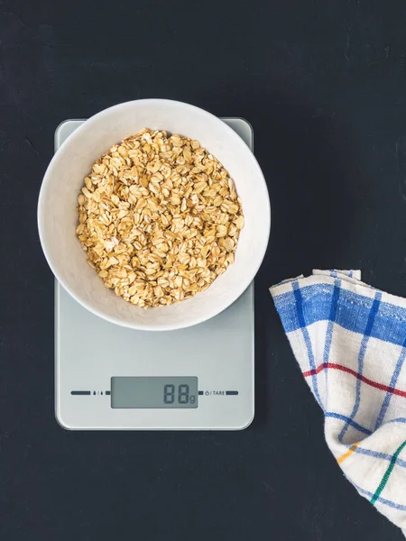 Diyet kavramı, doğru beslenme, sağlıklı yemek. Yulaf ezmesi mutfak terazisi üzerinde beyaz bir tabak içinde. Ürünler ağırlığında. Kahvaltı, üstten görünüm