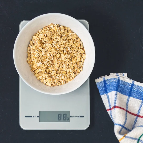 Diyet kavramı, doğru beslenme, sağlıklı yemek. Yulaf ezmesi mutfak terazisi üzerinde beyaz bir tabak içinde. Ürünler ağırlığında. Kahvaltı, üstten görünüm
