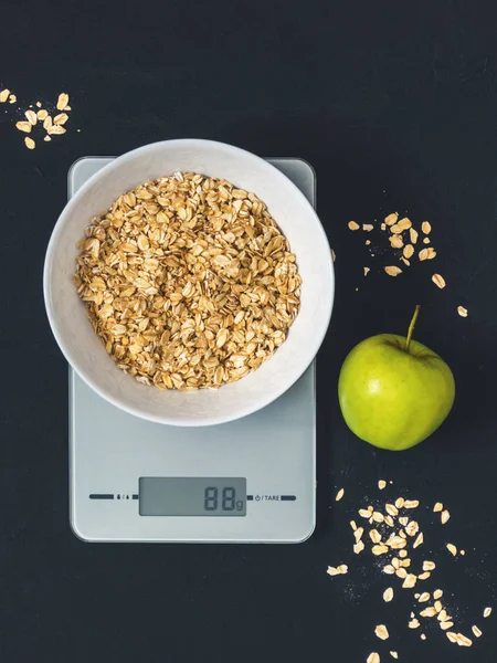 Diyet kavramı, doğru beslenme, sağlıklı yemek. Yulaf ezmesi mutfak terazisi üzerinde beyaz bir tabak içinde. Ürünler ağırlığında. Kahvaltı, üstten görünüm
