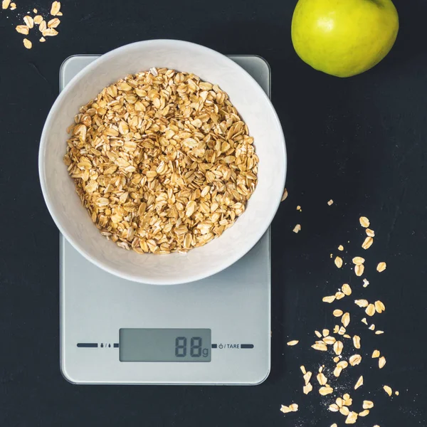 Diyet kavramı, doğru beslenme, sağlıklı yemek. Yulaf ezmesi mutfak terazisi üzerinde beyaz bir tabak içinde. Ürünler ağırlığında. Kahvaltı, üstten görünüm