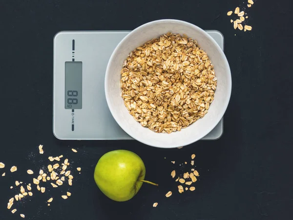Diyet kavramı, doğru beslenme, sağlıklı yemek. Yulaf ezmesi mutfak terazisi üzerinde beyaz bir tabak içinde. Ürünler ağırlığında. Kahvaltı, üstten görünüm