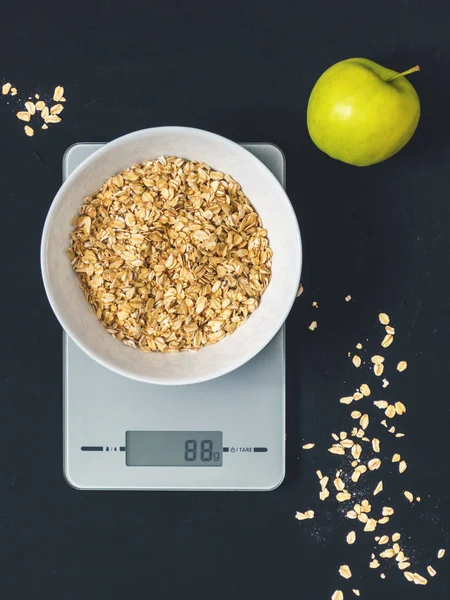 Diyet kavramı, doğru beslenme, sağlıklı yemek. Yulaf ezmesi mutfak terazisi üzerinde beyaz bir tabak içinde. Ürünler ağırlığında. Kahvaltı, üstten görünüm