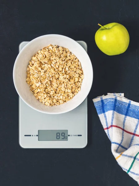 Diyet kavramı, doğru beslenme, sağlıklı yemek. Yulaf ezmesi mutfak terazisi üzerinde beyaz bir tabak içinde. Ürünler ağırlığında. Kahvaltı, üstten görünüm