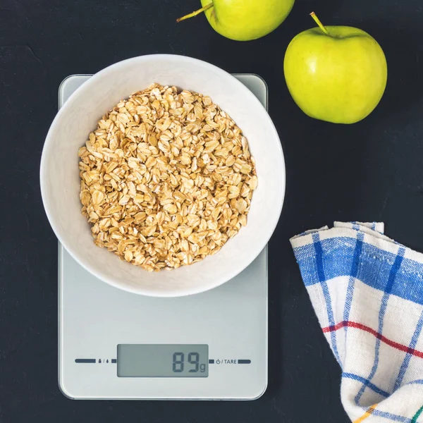 Diyet kavramı, doğru beslenme, sağlıklı yemek. Yulaf ezmesi mutfak terazisi üzerinde beyaz bir tabak içinde. Ürünler ağırlığında. Kahvaltı, üstten görünüm