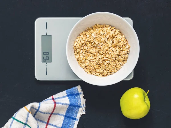 Diyet kavramı, doğru beslenme, sağlıklı yemek. Yulaf ezmesi mutfak terazisi üzerinde beyaz bir tabak içinde. Ürünler ağırlığında. Kahvaltı, üstten görünüm