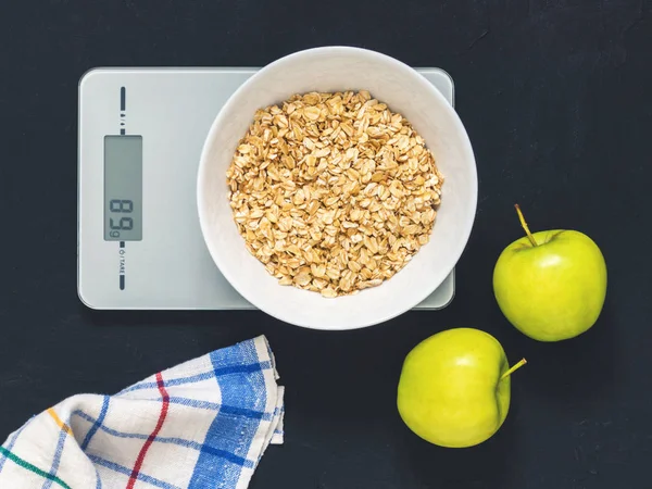 Diyet kavramı, doğru beslenme, sağlıklı yemek. Yulaf ezmesi mutfak terazisi üzerinde beyaz bir tabak içinde. Ürünler ağırlığında. Kahvaltı, üstten görünüm