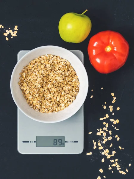 Diyet kavramı, doğru beslenme, sağlıklı yemek. Yulaf ezmesi mutfak terazisi üzerinde beyaz bir tabak içinde. Ürünler ağırlığında. Kahvaltı, üstten görünüm