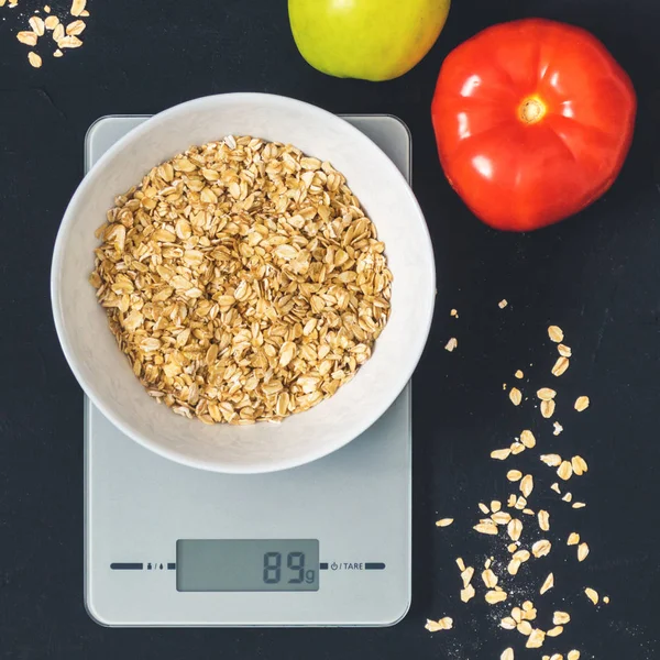 Diyet kavramı, doğru beslenme, sağlıklı yemek. Yulaf ezmesi mutfak terazisi üzerinde beyaz bir tabak içinde. Ürünler ağırlığında. Kahvaltı, üstten görünüm