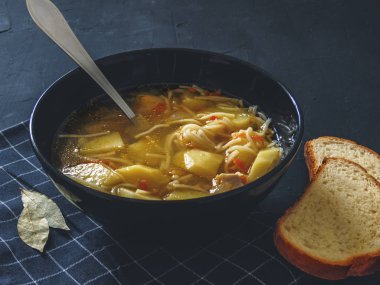 Patates, erişte, soğan, havuç ve iki parça ekmek siyah bir arka plan ile tavuk çorbası.
