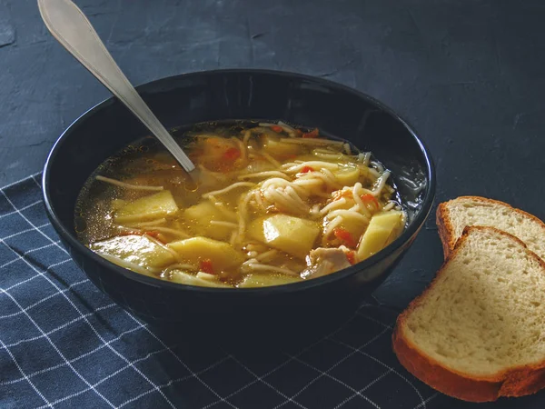 Patates, erişte, soğan, havuç ve iki parça ekmek siyah bir arka plan ile tavuk çorbası.