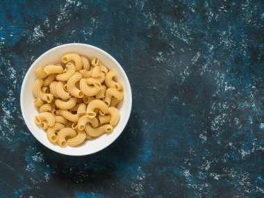 Mavi grunge arka plan üzerinde beyaz tabak çeşitli kuru makarna. Üstten görünüm. Kopya alanı