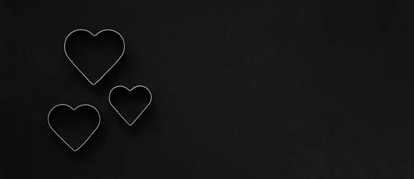 Metal hearts on a festive black background. Baking molds. Cookie cutters. Flat lay, top view