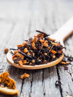 Ahşap arka plan üzerinde siyah meyve çay tarçın, elma, portakal, kişniş, kakule, karanfil ve tahta kaşık kırmızı biber ile kuru yapraklar