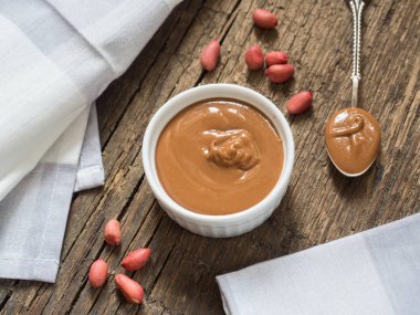 Ahşap bir masa üzerinde beyaz bir kase fıstık ezmesi. Doğal sağlıklı beslenme ve organik gıda