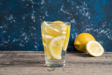 Taze temiz su bir bardak limon dilimleri ile. Ahşap masa ve mavi arka plan limonata. Su yaşam, sağlıklı içecek