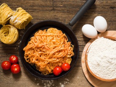 Ahşap bir masa üzerinde siyah bir tavada domates sosu ve fesleğen ile iştah açıcı geleneksel klasik İtalyan makarna. Düz yatıyordu