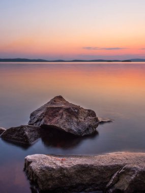 Sakin ve meditasyon kavramı. Gölde gün batımı, ön plandaki kayalar, sessiz su, bulutsuz gökyüzü