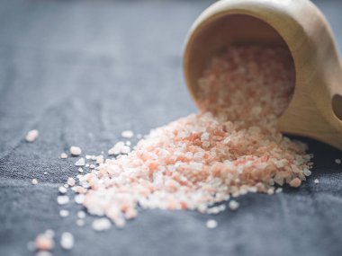 Yararlı baharatkavramı. Tahta bir bardaktan siyah bir masa örtüsüne dökülen büyük koyu pembe himalaya tuzu. Closeup