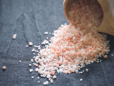 Yararlı baharatkavramı. Tahta bir bardaktan siyah bir masa örtüsüne dökülen büyük koyu pembe himalaya tuzu. Closeup