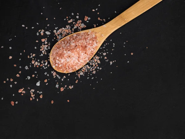 Sağlıklı baharat kavramı. Tahta bir kaşık büyük koyu pembe himalaya tuzu ve siyah bir masaya döküldü. Closeup