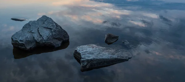 Sakin, dinginlik, meditasyon konsepti. Gölde gün batımı, ön plandaki sudaki taşlar, sessiz su, bulutsuz gökyüzü. Mavi saat