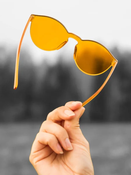 Концепція кольорового способу життя. Помаранчеві сонцезахисні окуляри в жіночій руці на сірому фоні — стокове фото