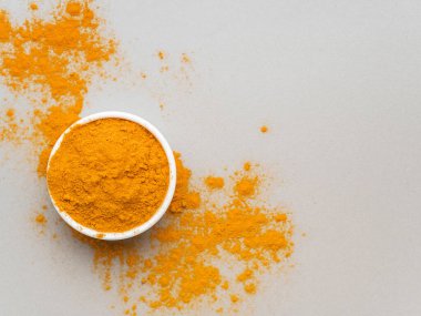 Zerdeçal tozu. Geleneksel Hint altın sarısı baharatı beyaz seramik kasede gri arka planda. Üst görünüm
