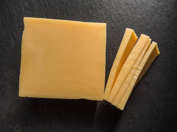 Queso parmesano en rodajas rectangulares sobre una tabla de cortar de pizarra negra. Primer plano — Foto de Stock