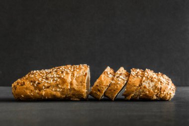 Kepekli taze pişmiş ekmek, keten ve siyah zemin üzerinde susam tohumları. Yan görünüm