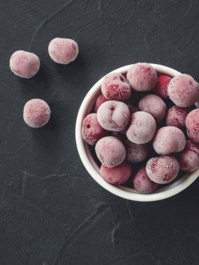 Siyah arka planda beyaz kasede donmuş taze kiraz çilekleri. Yakın plan. Üst görünüm