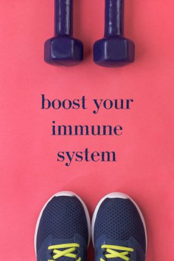 Bağışıklık sistemi posterinizi, spor ve aktif yaşam tarzınızı geliştirin. Mor koşu ayakkabıları ve pembe arka planda iki dambıl. Düz yatıyordu. Üst görünüm