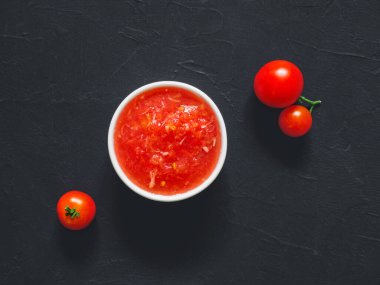 Siyah arka planda beyaz kasede taze olgun domateslerden yapılan ev yapımı domates sosu. Domates pizza ezmesi. Vejetaryen yemeği. Üst görünüm