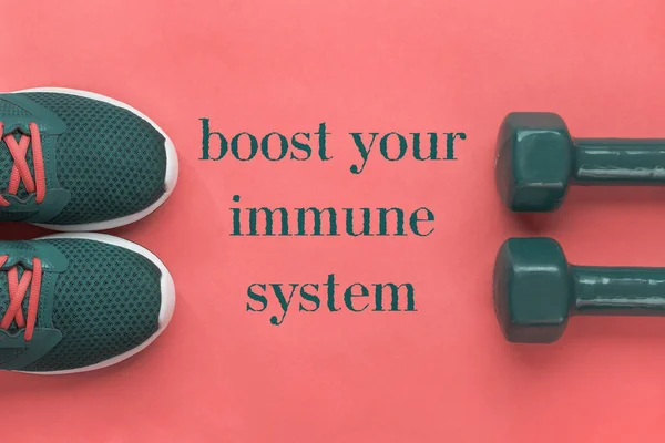 Aumenta tu sistema inmunológico: letras en banner, concepto deportivo. Zapatillas de running púrpura y dos mancuernas sobre fondo rosa — Foto de Stock