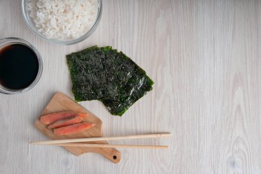 Taze çiğ somon dilimleri ahşap kesme tahtasının üzerinde duruyor. Mutfaktaki çubuklarla birlikte. Nori çarşafları ve beyaz pirinçle çevrili.