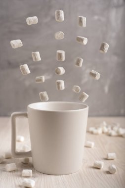 Mutfakta uçuşan beyaz şekerlemelerle çevrili açık ahşap masanın üzerinde duran basit, beyaz bir fincan.