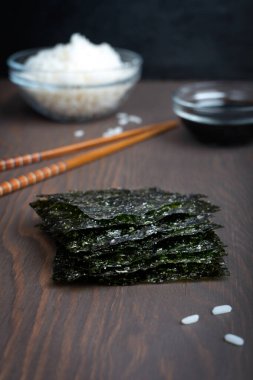 Kurumuş deniz yosunları yığını, yemek çubukları ve bir kase pirinçle çevrili koyu ahşap masanın üzerinde yatıyor.