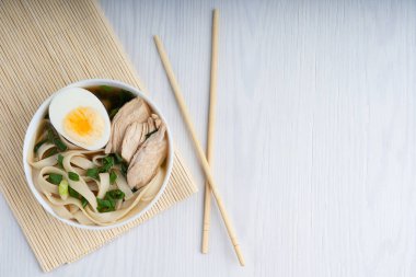 Baharatlı ramen çorbası soya soslu tavuk çorbası ve yarım yumurta ve et dilimleri ile süslenmiş erişte. Beyaz ahşap bir masada yemek çubuklarıyla birlikte. Kopyalama alanı olan resim