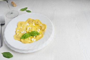 İtalyan ravioli makarnası ricotta peyniri ve fesleğen yapraklarıyla süslenmiş, etrafı çatalla çevrili, beyaz ahşap zemin üzerinde bir bardak şarap ve ıspanak yemeye hazır. Kopyalama alanı olan resim