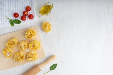 Fırınlanmamış İtalyan fettucine makarnasının üst görüntüsü. Kesme tahtasındaki un ve domateslerle çevrili tekerlekli pim ve peçete ve zeytinyağının üzerine ıspanak. Kopyalama alanı ve yatay yönelimli resim