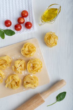 Kesme tahtasında çiğ İtalyan fettucine makarna ve domateslerle çevrili pim ve havluda ıspanak ve mutfakta beyaz ahşap arka planda zeytinyağı soslu tekne. Dikey yönelim