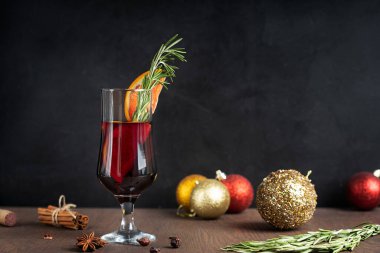 Bir bardak sıcak baharatlı kırmızı şarap genellikle soğuk kış akşamlarında hazırlanmış biberiye ile süslenmiş Noel süslemeleri, baharatlar, anason yıldızı ve siyah ahşap masa üzerinde tarçın demeti.