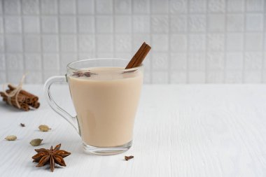 Sıcak Hint masala çayı ya da sütle yapılan karışık baharat çayı ve anason ve tarçın gibi çeşitli aromatik otlar mutfakta beyaz ahşap arka planda cam bardakta. Kopyalama alanı olan resim