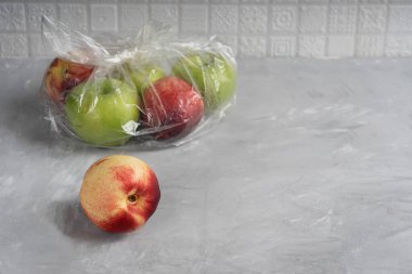 Mutfaktaki plastik veya polietilen şeffaf torba dolusu elma ve nektarin, çevresel kirlilik küresel sorununu gösteriyor. Kopyalama alanı olan resim