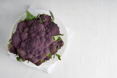 Leylak karnabahar ya da mor brokoliyle bembeyaz bir tabakta, ahşap zemin üzerinde yemek pişirmeye hazır halde yatıyordu. Kopyalama alanı ve yatay yönelimli resim