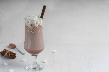 Sıcak geleneksel kakao içeceği uzun bardakta marşmelov ve tarçın çubuğu beyaz ahşap arka planda genellikle soğuk kış aylarında hazırlanır. Kopyalama alanı ve yatay yönelimli resim